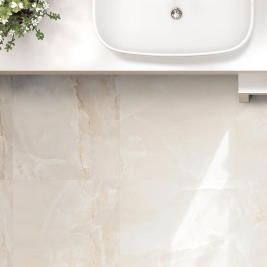 An elegant bathroom wall featuring a beige onyx ceramic tile with a glossy finish, installed in a setting with a white sink and wooden accessories.